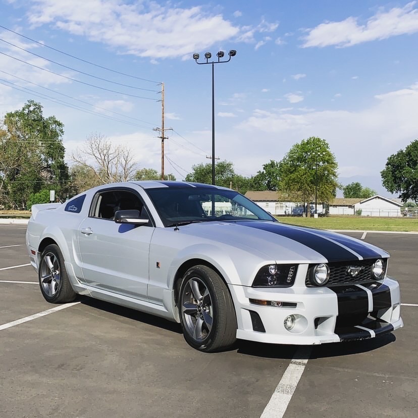 A white Mustang with black racing stripes parked in an open lot