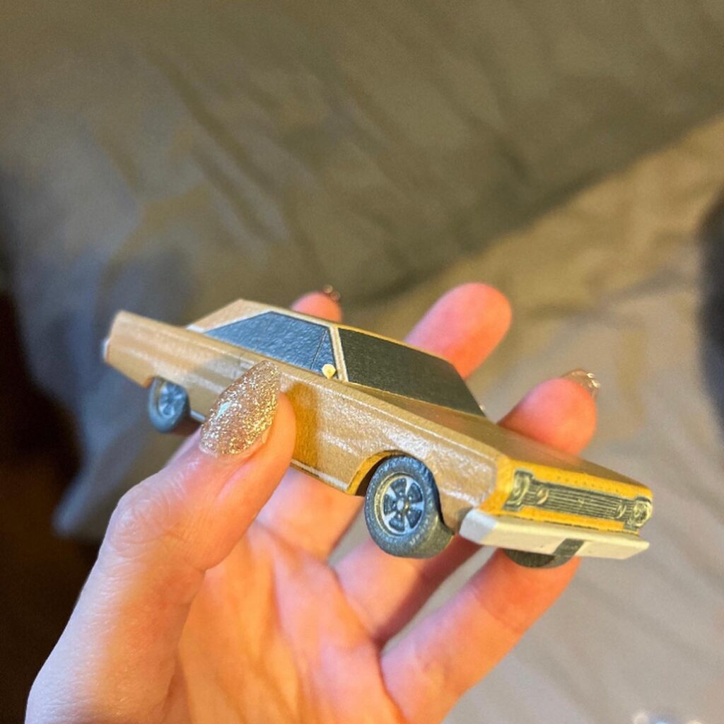  A hand holding a custom 3D-printed classic car model, replicating a real vintage Plymouth.